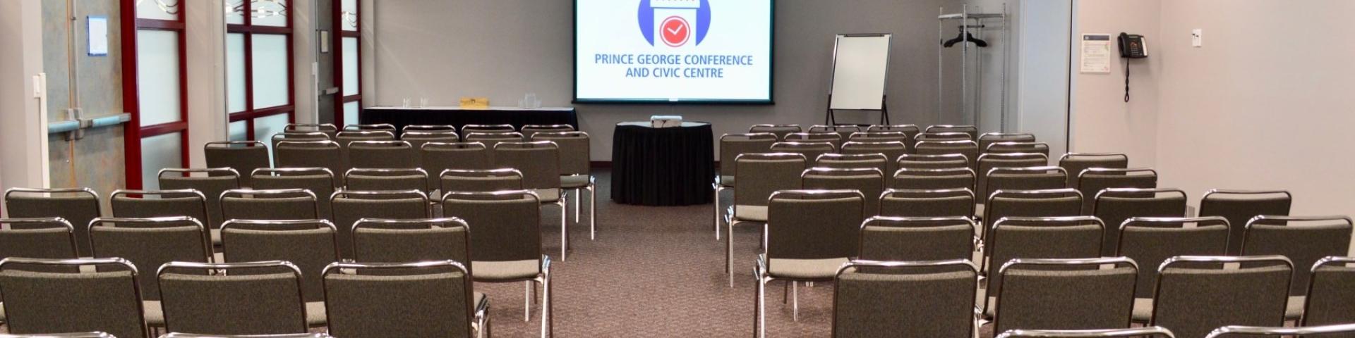 Rows of chairs in meeting room, facing projector screen on far wall