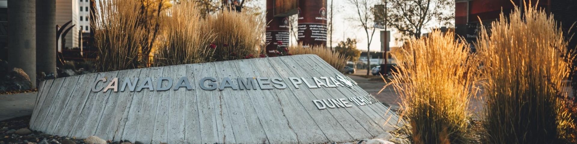 Metal text that reads "Canada Games Plaza" written on cement protrusion in garden area